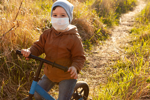 A boy rides a balance bike in a clearing. A boy in a protective mask - 写真・画像