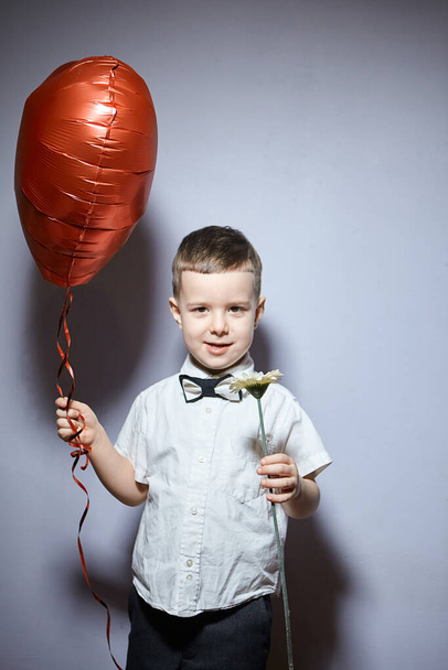 Día de San Valentín. Niño feliz se para y sostiene corazones de bola roja sobre un fondo blanco.  - Foto, Imagen
