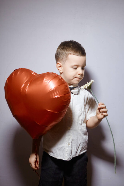 Valentine's day. Happy boy stands and holds red ball hearts on a white background.  - Foto, Imagen