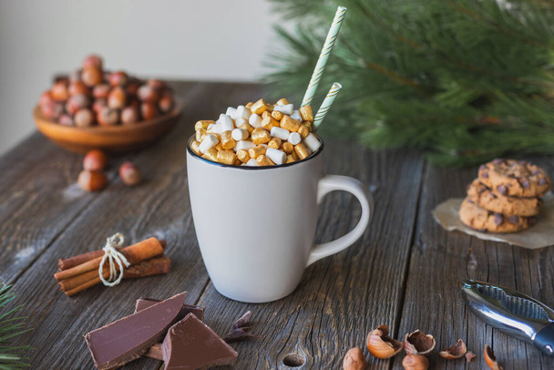 A mug of hot chocolate or cocoa, decorated with gold and white marshmallows, on a wooden table. Place for your text. Hot autumn and winter drink - Photo, Image