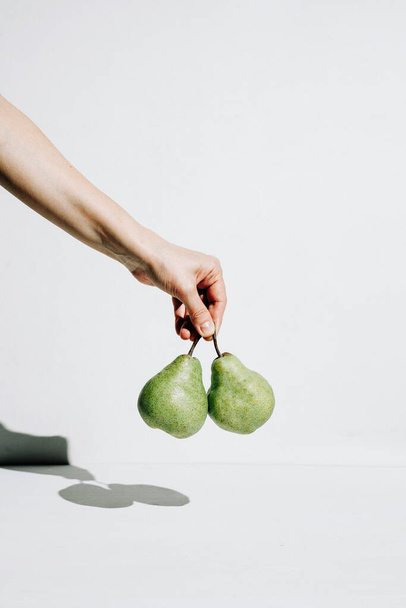 Woman's hand holds 2 pears on white background, minimalism concept, healthy food, vitamins and vegetarianism concept. Top view, flat lay - Photo, Image