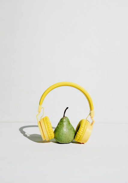 The music player in the shape of an pear with headphones. Fantasy on the theme of music and fruits, podcast for a healthy lifestyle - Foto, immagini