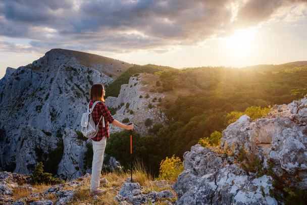 Подходит женщина-туристка с рюкзаком и шестами, стоящая на скалистом горном хребте, выглядывая наружу, и персиками в концепции здорового образа жизни на открытом воздухе - Фото, изображение