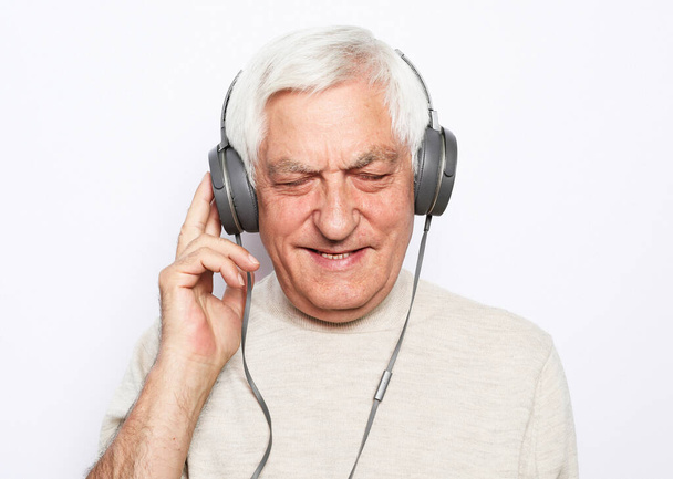Lifestyle, tehnology and old people concept: image of an elderly gray-haired man listening to music with headphones over white background - Фото, зображення