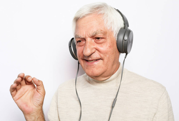 Lifestyle, tehnology and old people concept: image of an elderly gray-haired man listening to music with headphones over white background - Fotoğraf, Görsel