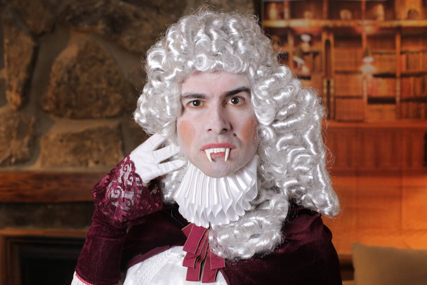 Молодий чоловік у вікторіанському костюмі з вампірськими зубами, що сидять у приміщенні. - Фото, зображення