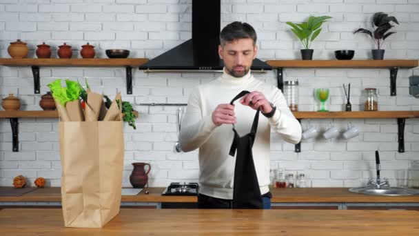 Homme en pull vient à la maison cuisine met sur tablier préparation des aliments sains cuisinier - Séquence, vidéo