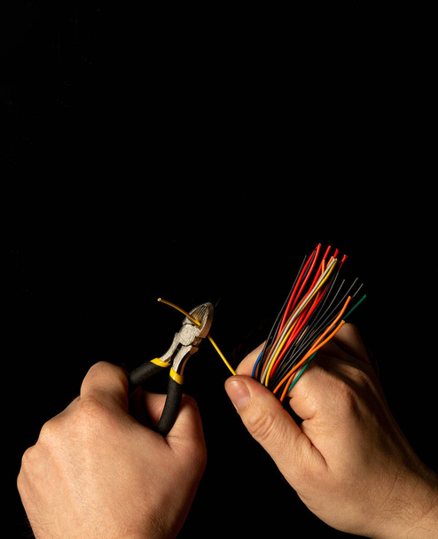 Hände des Meisters halten Drahtschneider und Drahtnahaufnahmen auf schwarzem Hintergrund. Elektronische Reparatur-Idee - Foto, Bild