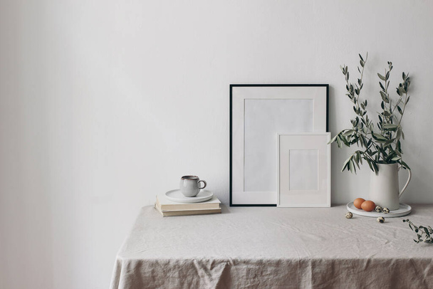 Spring, Easter breakfast still life. Cup of coffee, books and empty picture frames mockups. Linen tablecloth. Olive tree branches in ceramic jug. Hen, quail eggs. Farmhouse, Scandinavian interior. - Фото, изображение