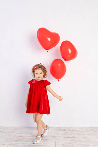 girl with heart-shaped balloons in a red dress on a white background, the concept of love and Valentine's day - Foto, afbeelding