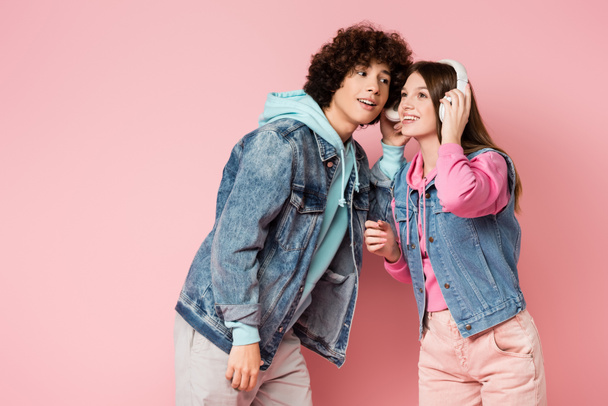 Cheerful teenagers listening music in headphones on pink background - Photo, Image