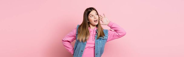 Teenager with hand near ear looking away on pink background, banner  - Photo, Image