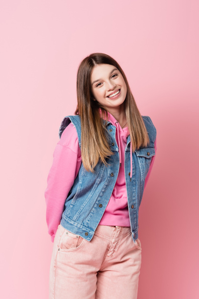Lächelndes Teenager-Mädchen blickt in die Kamera auf rosa Hintergrund - Foto, Bild
