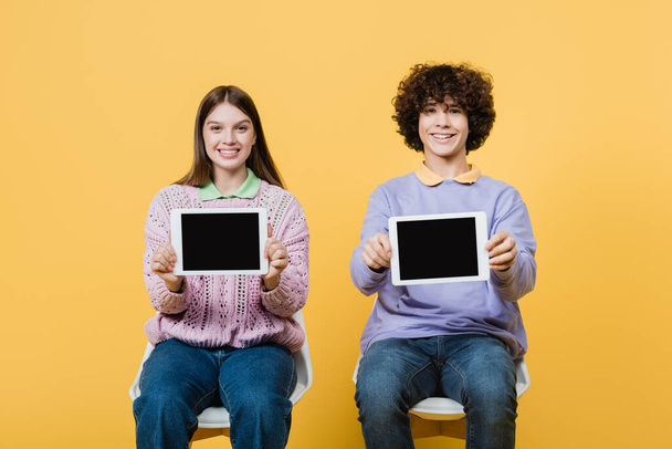 Pozitivní teenageři zobrazující digitální tablety na žlutém pozadí - Fotografie, Obrázek