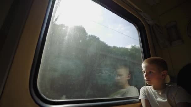 El chico mira por la ventana del tren. El chico viaja en tren. Tren de carga entrante fuera de la ventana del pasajero. El niño sueña con unas divertidas vacaciones de verano. Viaje familiar de larga distancia. Fin del bloqueo. - Metraje, vídeo