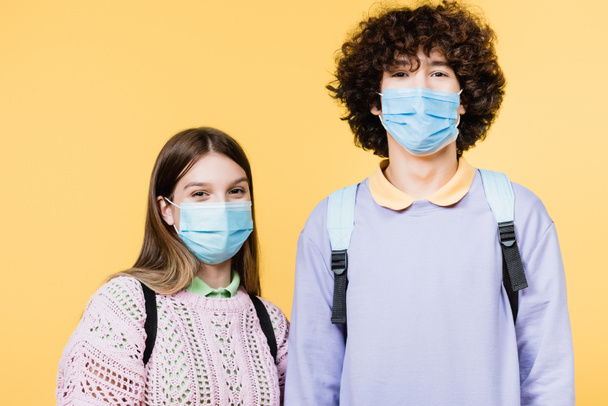 Teenagers in medical masks looking at camera isolated on yellow - Fotó, kép
