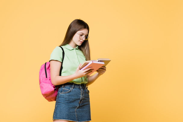 Chica en gafas con mochila libro de lectura aislado en amarillo - Foto, Imagen