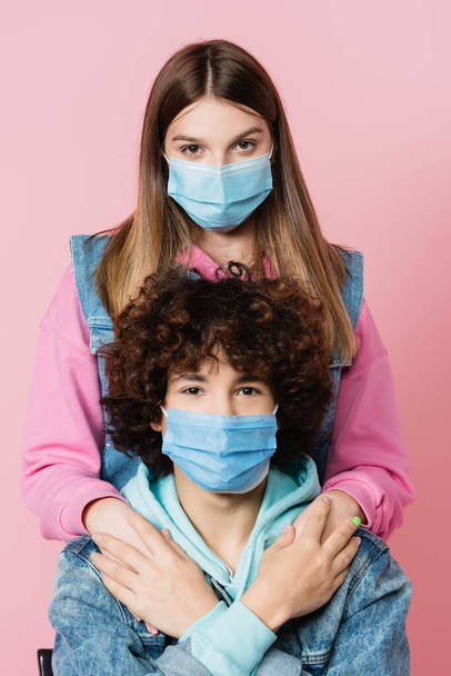 Meisje in medisch masker hand in hand van vriendje geïsoleerd op roze  - Foto, afbeelding