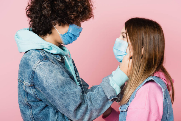 Пара подростков в медицинских масках, смотрящих друг на друга в розовом  - Фото, изображение