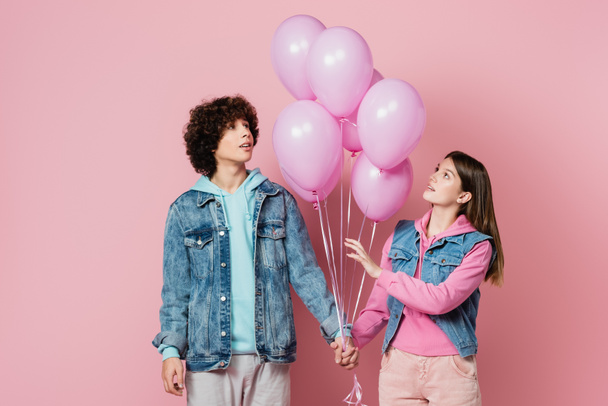 Adolescentes tomados de la mano mientras miran globos sobre fondo rosa  - Foto, imagen