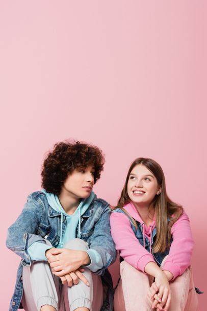 Curly teenager looking at smiling girlfriend on pink background - Fotoğraf, Görsel