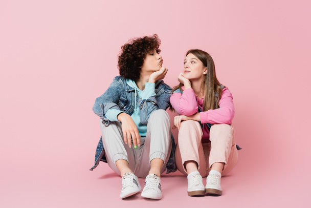 Curly teenager pouting lips near girlfriend on pink background - Foto, imagen