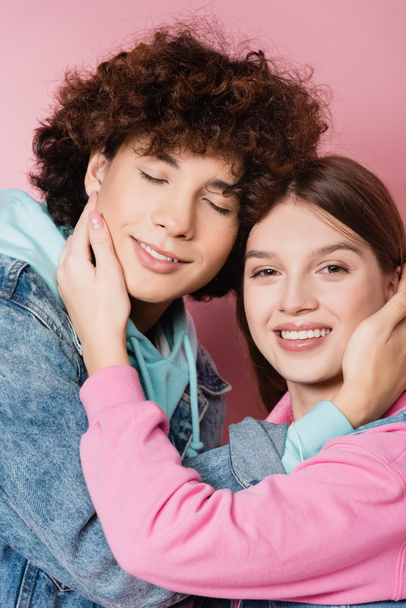 Cheerful teenagers touching faces of each other on pink background - Photo, Image