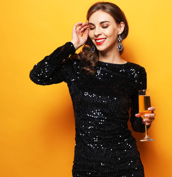 Young stylish woman drinking champagne, celebrating new year, wearing evening dress. Happy New Year to you. One young and beautiful woman dancing with glass of champagne and smiling. Party time. - Foto, imagen