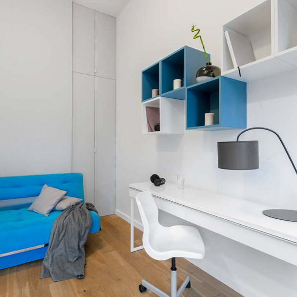 Simple decorated white and blue teenager room with desk to study, blue couch and modern square shelves - Fotoğraf, Görsel