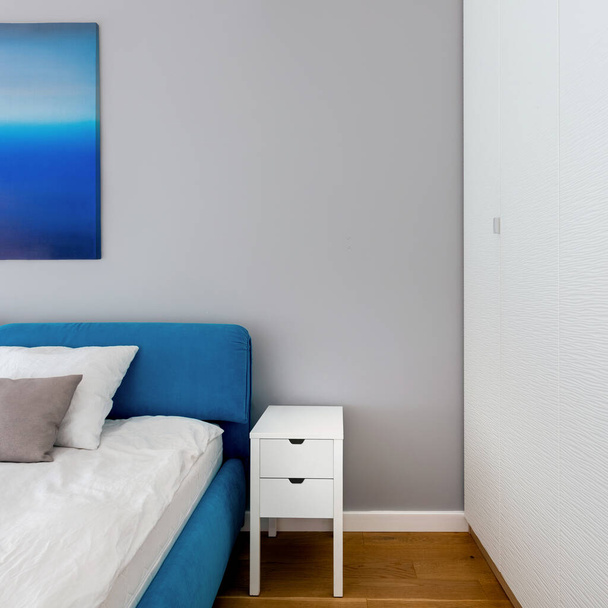 Close-up on simple white bedside table in bedroom with white wardrobe and blue bed - Foto, immagini