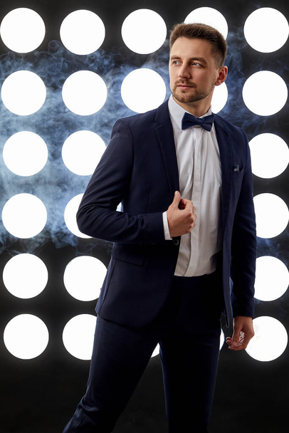 handsome man in tuxedo posing against the backdrop of spotlights - Foto, Imagen