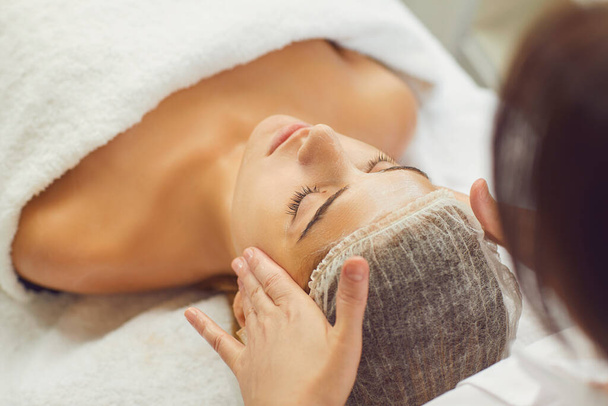 Face massage. Close-up of young woman getting spa massage treatment at beauty spa salon. - Fotó, kép