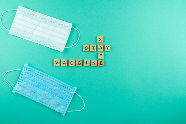 Words Covid Vaccine stay safe. The phrase is laid out in wooden letters. Top view. Motivation. Medical masks. Blue background. Mask. Copy space. Card. - Foto, afbeelding