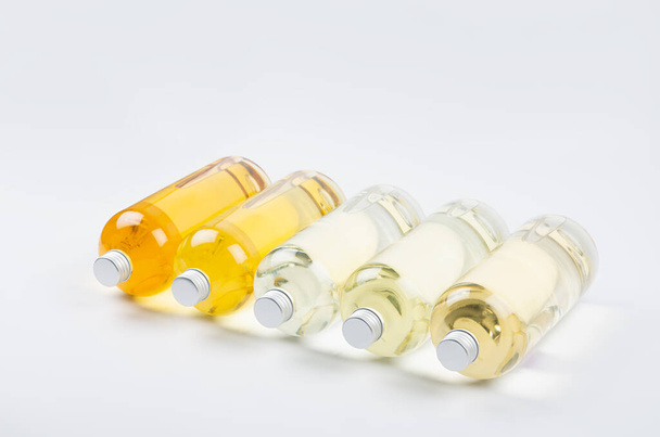 Collection transparent lying bottles with different pale colors liquid, cosmetic product, perfume or drink and silver cap in diadonal row on white background, side view. - Foto, imagen