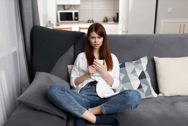 uma mulher com um telefone em suas mãos um olhar sério descansando em casa em um apartamento - Foto, Imagem
