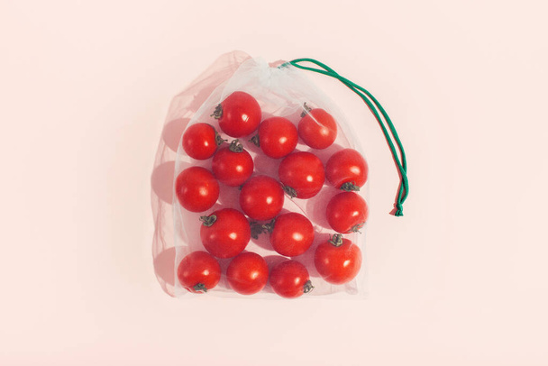 Mehrwegverpackungen von Produkten nach Gewicht. Rote Tomaten in einem Mehrwegbeutel in Großaufnahme auf rosa Hintergrund - Foto, Bild