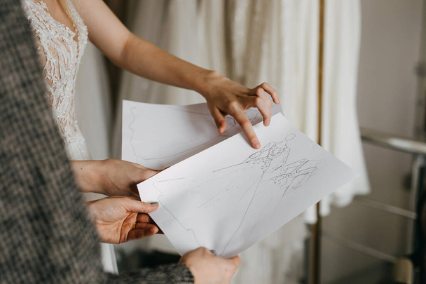 Designer de moda mostrando esboços de vestido de noiva para um cliente em seu estúdio. - Foto, Imagem
