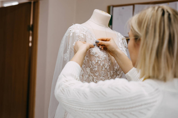 Nahaufnahme des Arbeitsprozesses einer Modedesignerin in ihrem Atelier. Handgenähtes Brautkleid Prozess. Pin Spitze auf einer Schaufensterpuppe Kleid.  - Foto, Bild