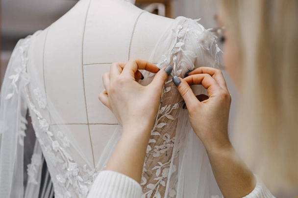 Primer plano del proceso de trabajo de una diseñadora de moda en su estudio. Costura a mano vestido de novia proceso. Pin encaje para vestir en un maniquí.  - Foto, Imagen