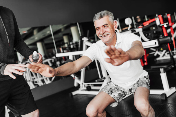 A retired man squats in the gym, he is cheerful and in good physical shape. - Foto, Imagem