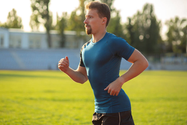 Closeup shot of a young muscular man with beard running outdoors at the park. Empty space - Photo, Image