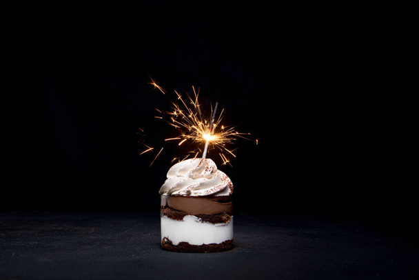 Delicious birthday cupcake with firework candle on table against dark background - Valokuva, kuva