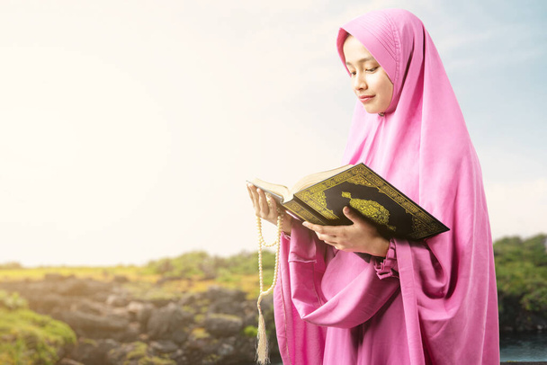 Asian Muslim woman in a veil holding prayer beads and reading the Quran at outdoor - Fotografie, Obrázek