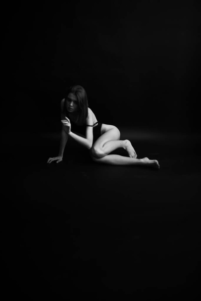 umělecká černobílá autentická fotografie štíhlé tanečnice v černém teplákovém obleku. Fotka autora studia. neobvyklé minimalistické pózy - Fotografie, Obrázek