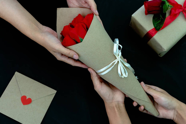 Közelkép a nők, akik egy csokor rózsát adnak ajándékdobozzal, kártya levél piros szívvel az asztalon, fekete háttér. Fogalom létrehozása kézzel készített ajándékok Valentin-napra vagy más nap ünnep - Fotó, kép