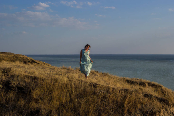 海のそばの崖の上に立っている長いドレスの少女 - 写真・画像