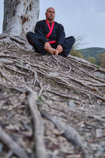Dövüş sanatları ustası siyah ve kırmızı kimonolu bir gölde meditasyon yapıyor. - Fotoğraf, Görsel