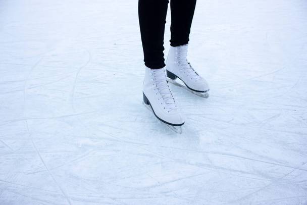 屋外のアイスリンクで白いフィギュアスケートで女性の足のクローズアップ。雪に覆われた冬の公園でスケートをしている若い女性 - 写真・画像