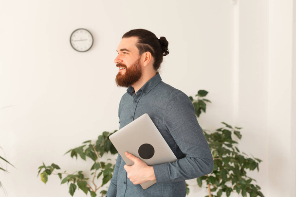 Portrait of young bearded man in office holding laptop - Photo, Image
