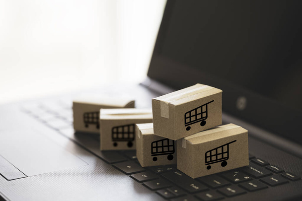 Trolley or shopping cart logo on small cartons boxes lay on keyboard computer laptop for online shopping and service delivery to customer concept. - 写真・画像